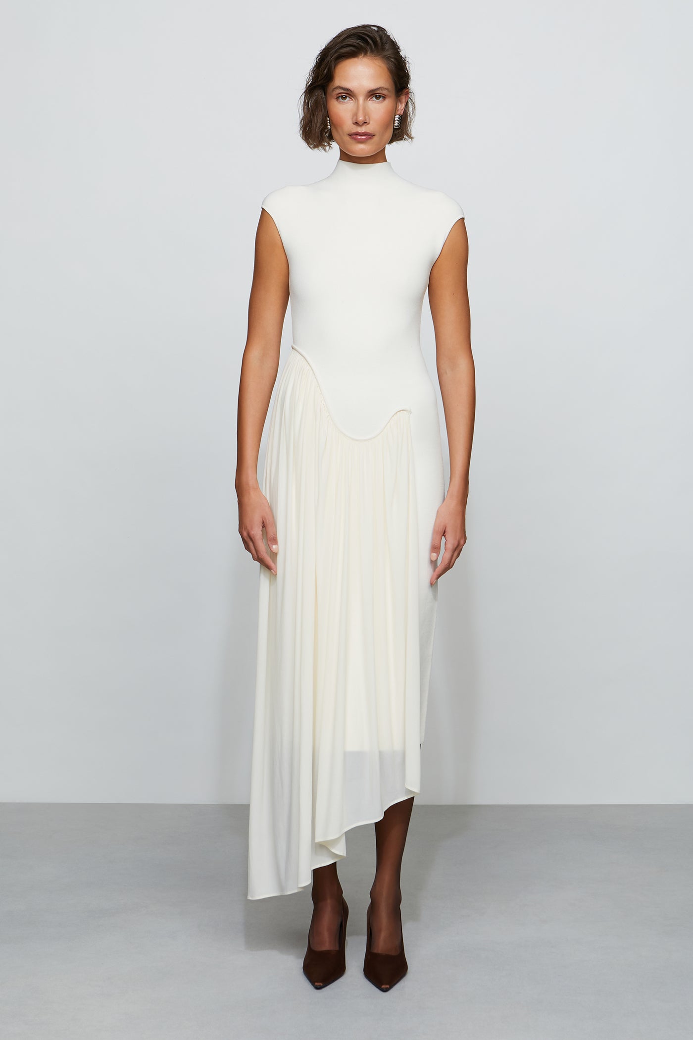 Woman wearing a white dress with a high neckline and pleated skirt on a plain background