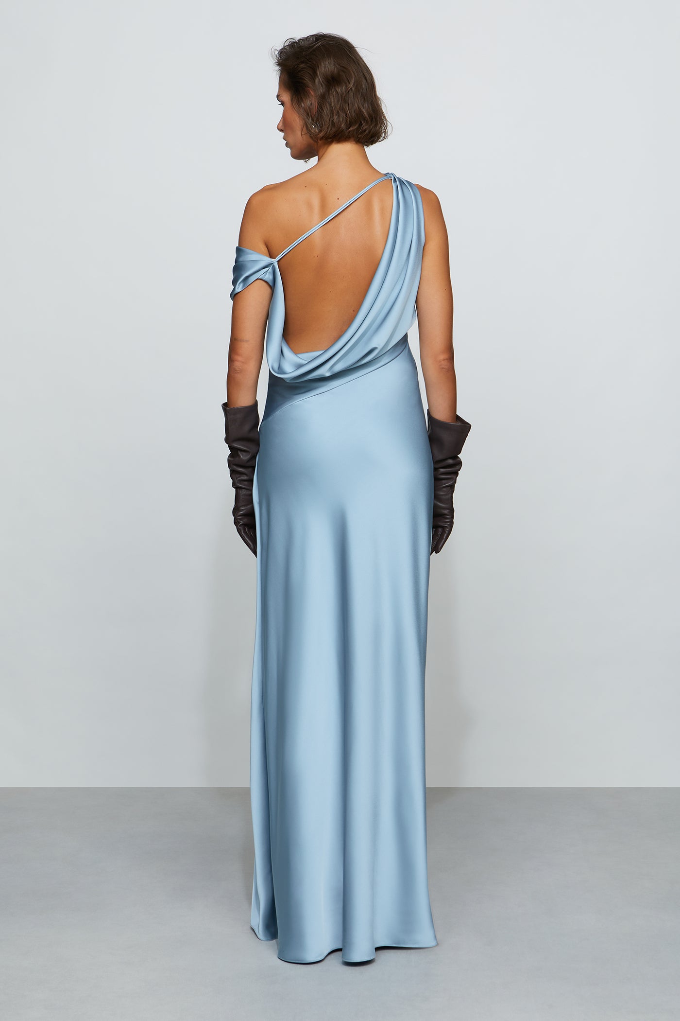 Woman wearing a light blue evening gown with a one-shoulder design on a plain background