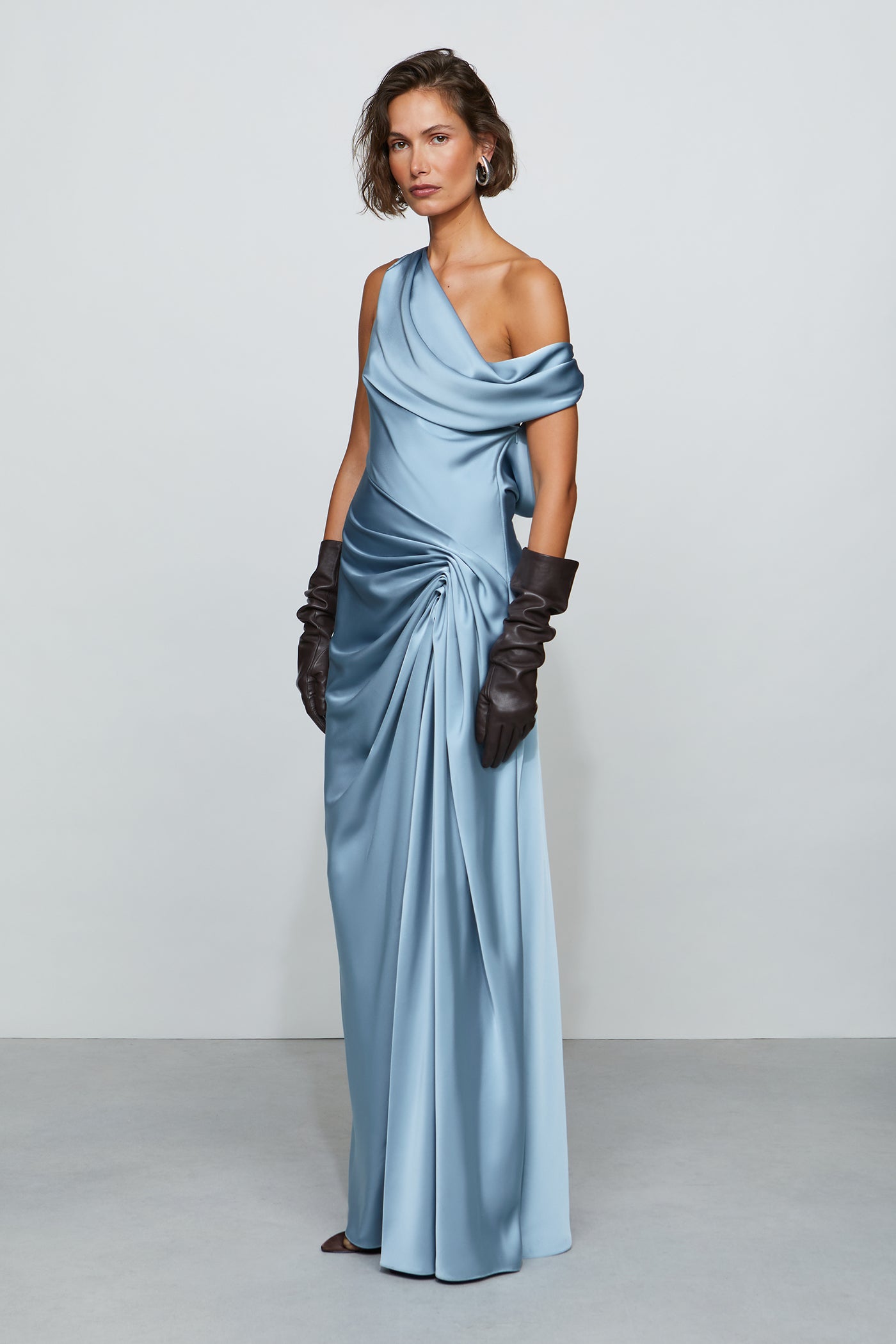 Woman wearing a light blue evening gown with gloves on a plain background
