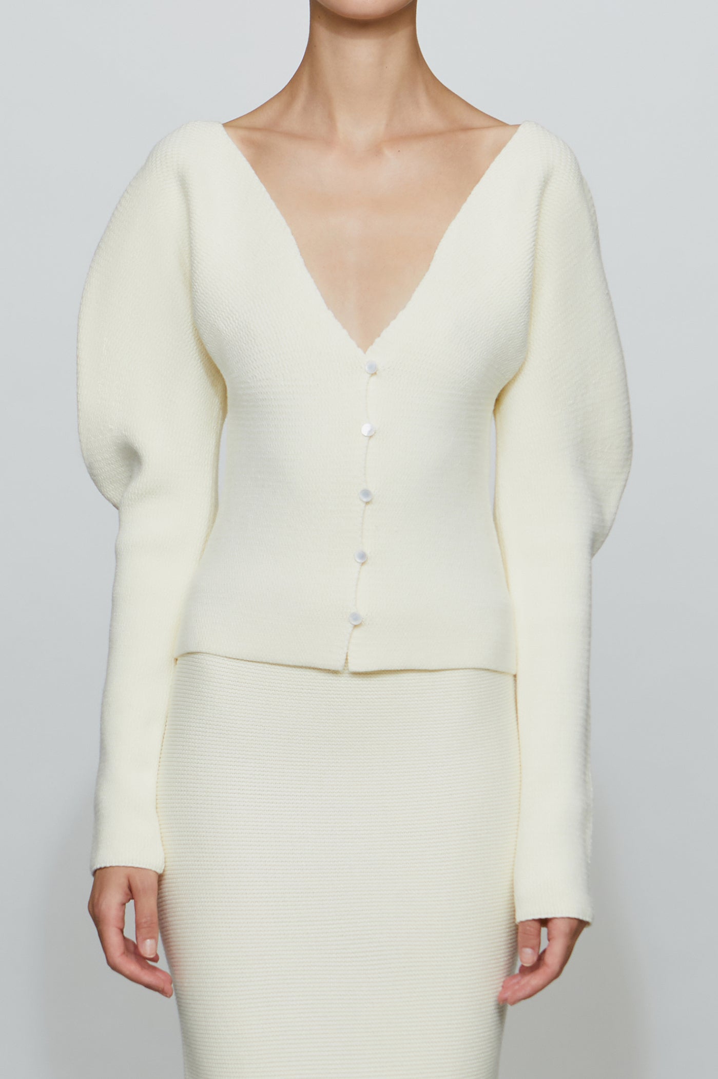 Cream-colored outfit with a cardigan and skirt on a plain background