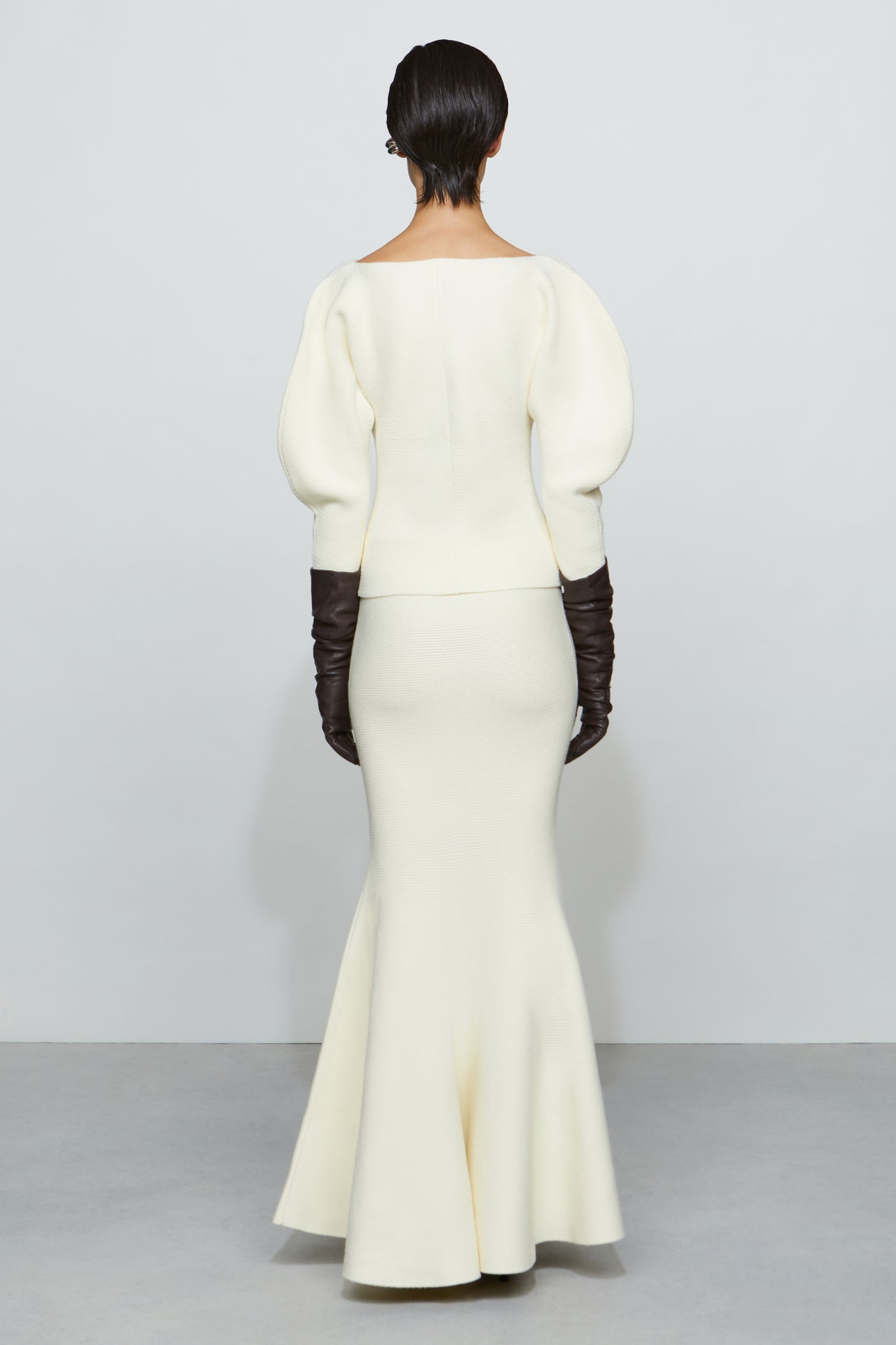 Woman wearing a white knit outfit with a fitted bodice and flared skirt on a plain background