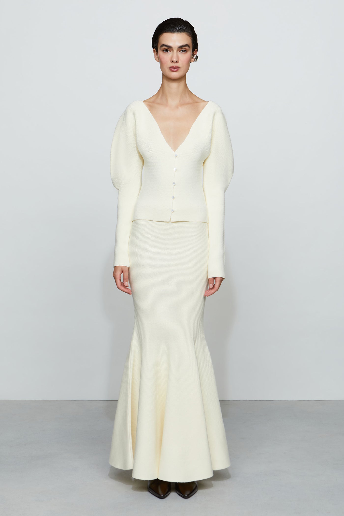 Woman wearing a white knit outfit with a fitted bodice and flared skirt on a plain background