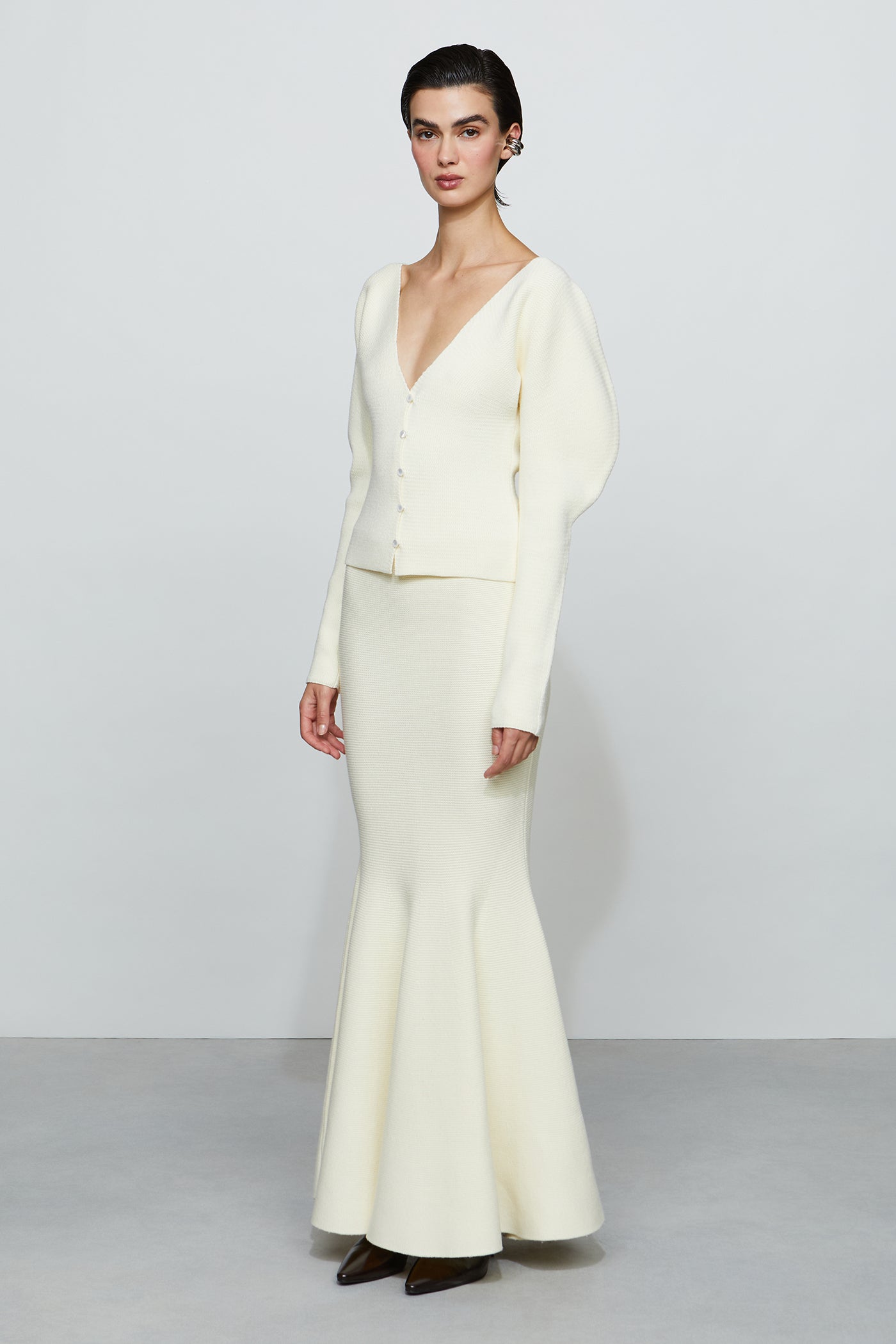 Woman wearing a white outfit with a fitted top and flared pants on a plain background