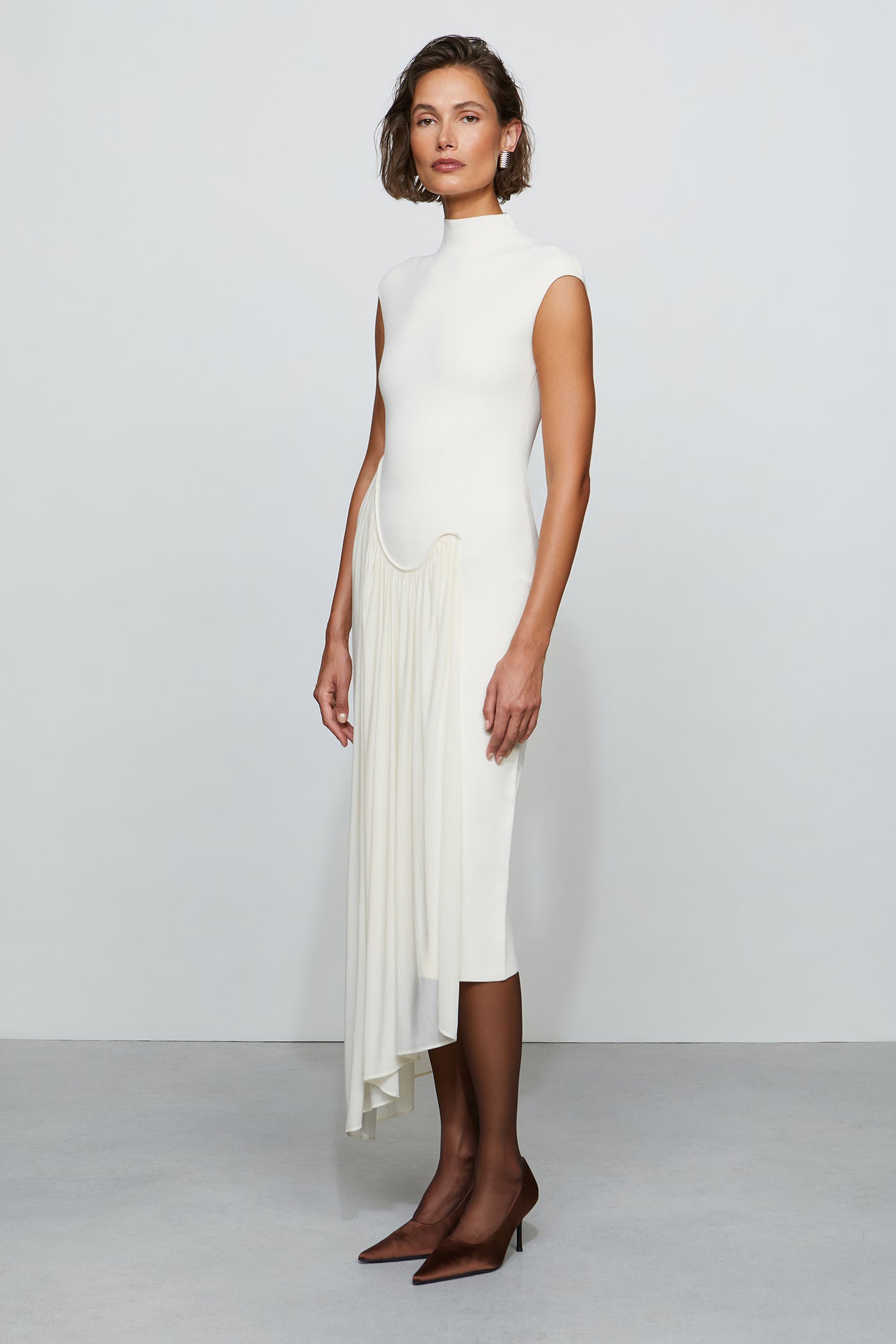 Woman wearing a white sleeveless dress with pleated skirt on a plain background