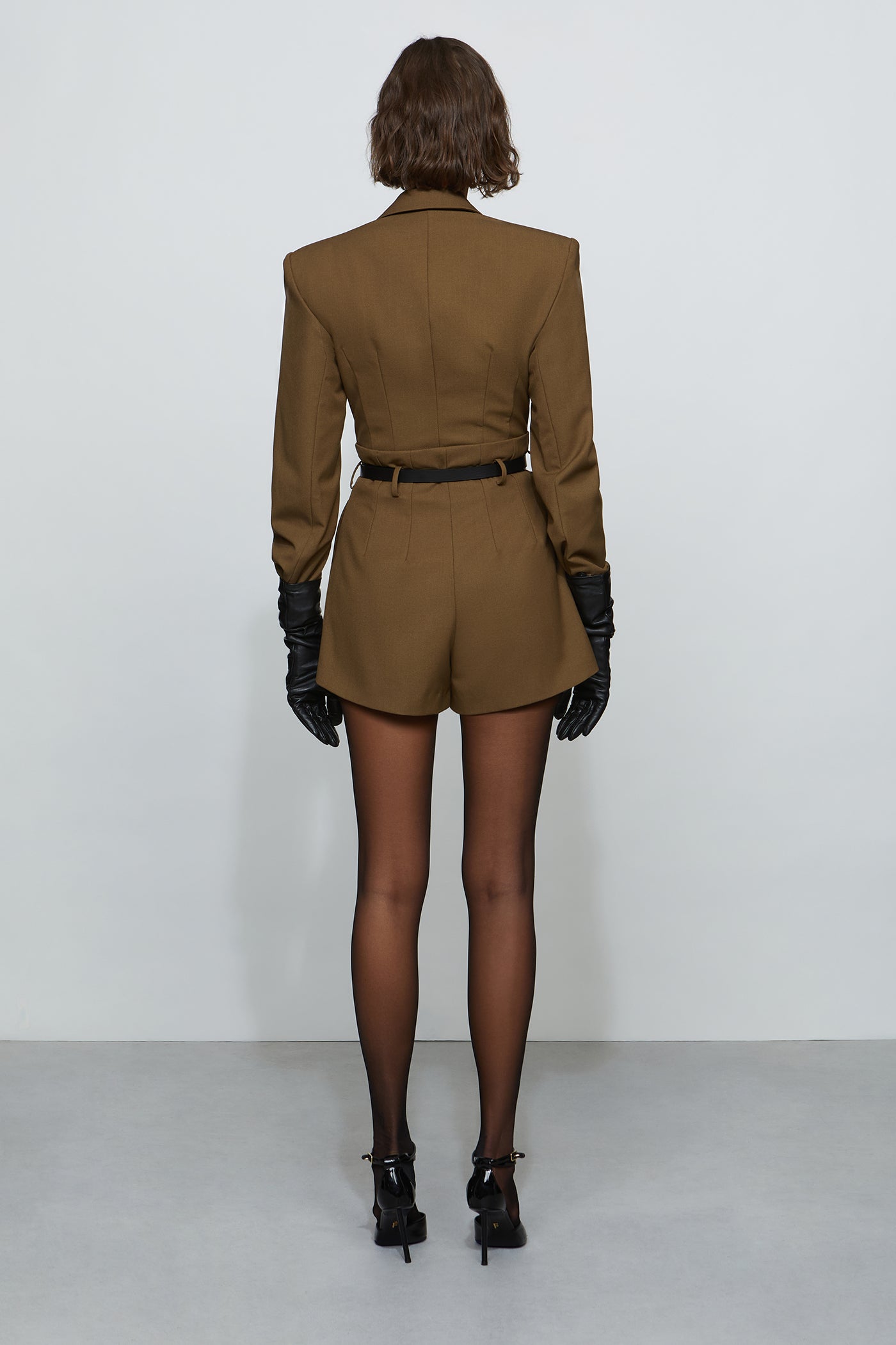 Woman wearing a brown suit with black gloves and shoes on a white background