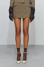 Person wearing a green plaid skirt, brown gloves, and high-heeled shoes on a white background