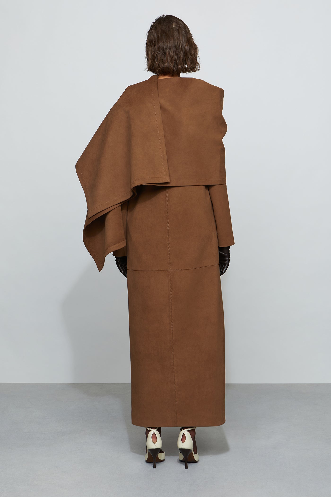 Person wearing a brown coat and skirt set against a white background